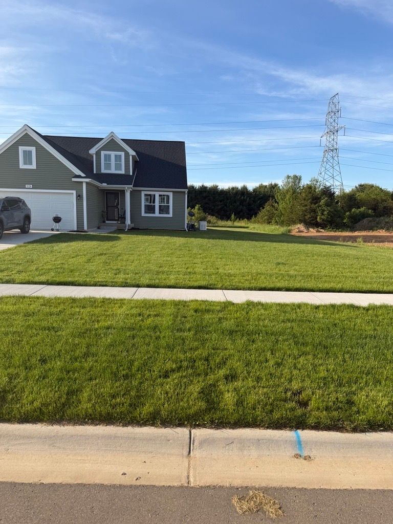 Suburban house with gray siding, green lawn, blue sky, and a utility tower in the background