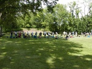 A group of people standing on a grassy field in front of a wooded area, likely at an outdoor range or park.