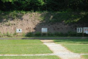 A grassy outdoor shooting range with paper targets set up in front of an earthen backstop.