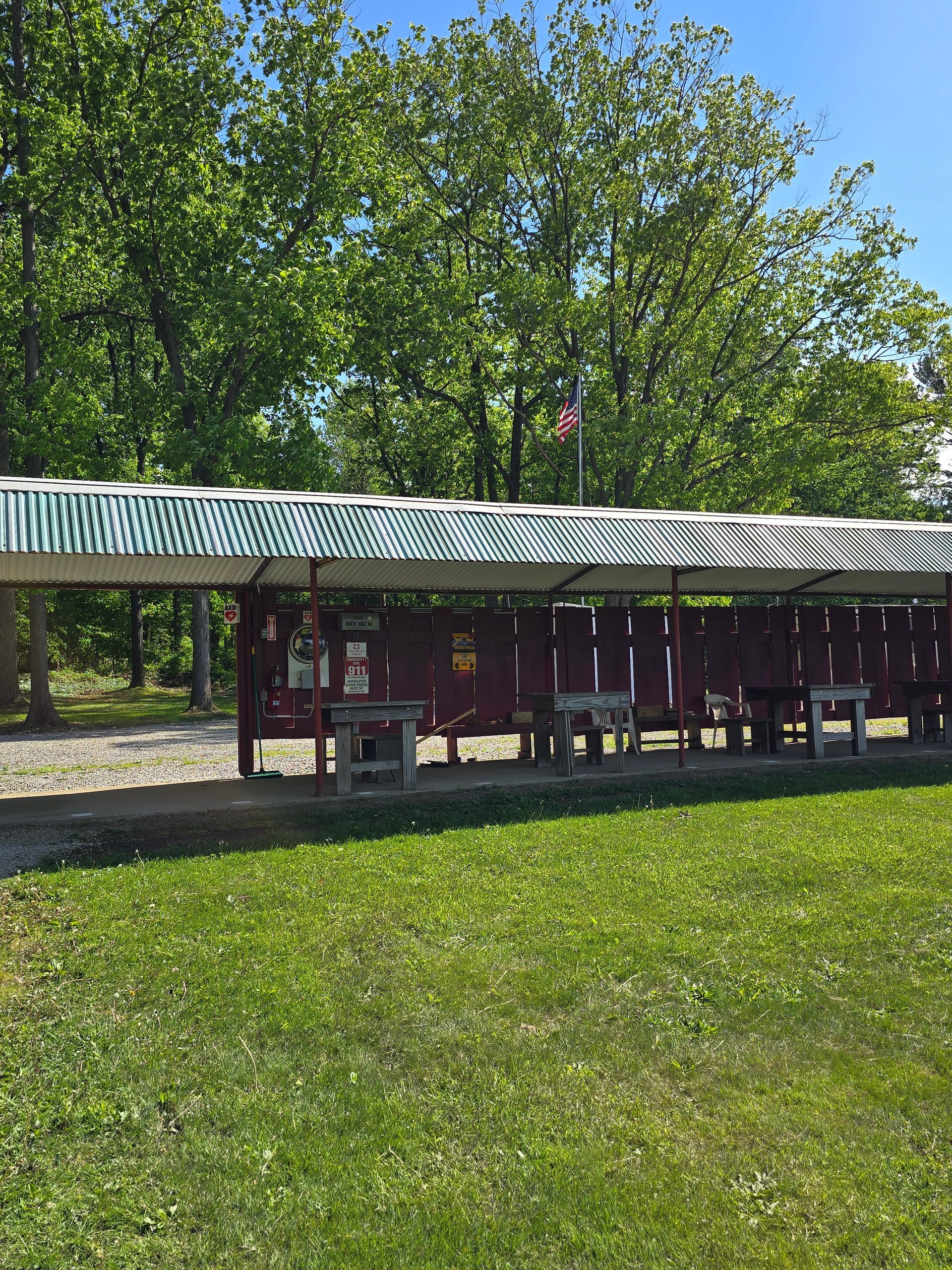 A covered outdoor shooting range with wooden benches, a maroon wall, and a green and white striped awning in a forest.
