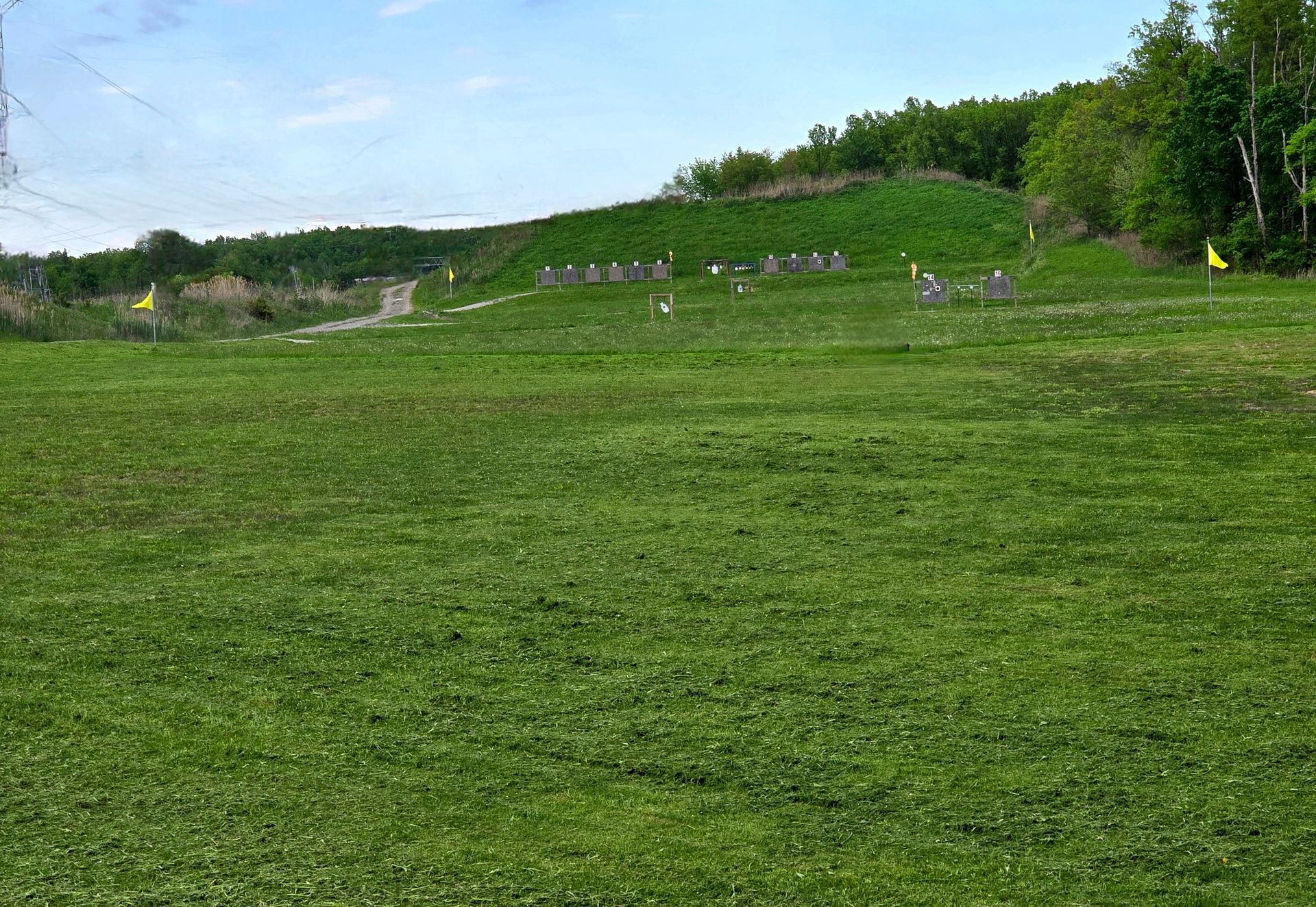 An outdoor shooting range with target stands set against a green, grassy hillside under a blue sky.