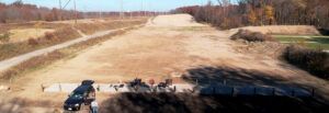 An aerial view of an outdoor shooting range with a concrete firing line, a vehicle, and a large, open dirt firing lane.