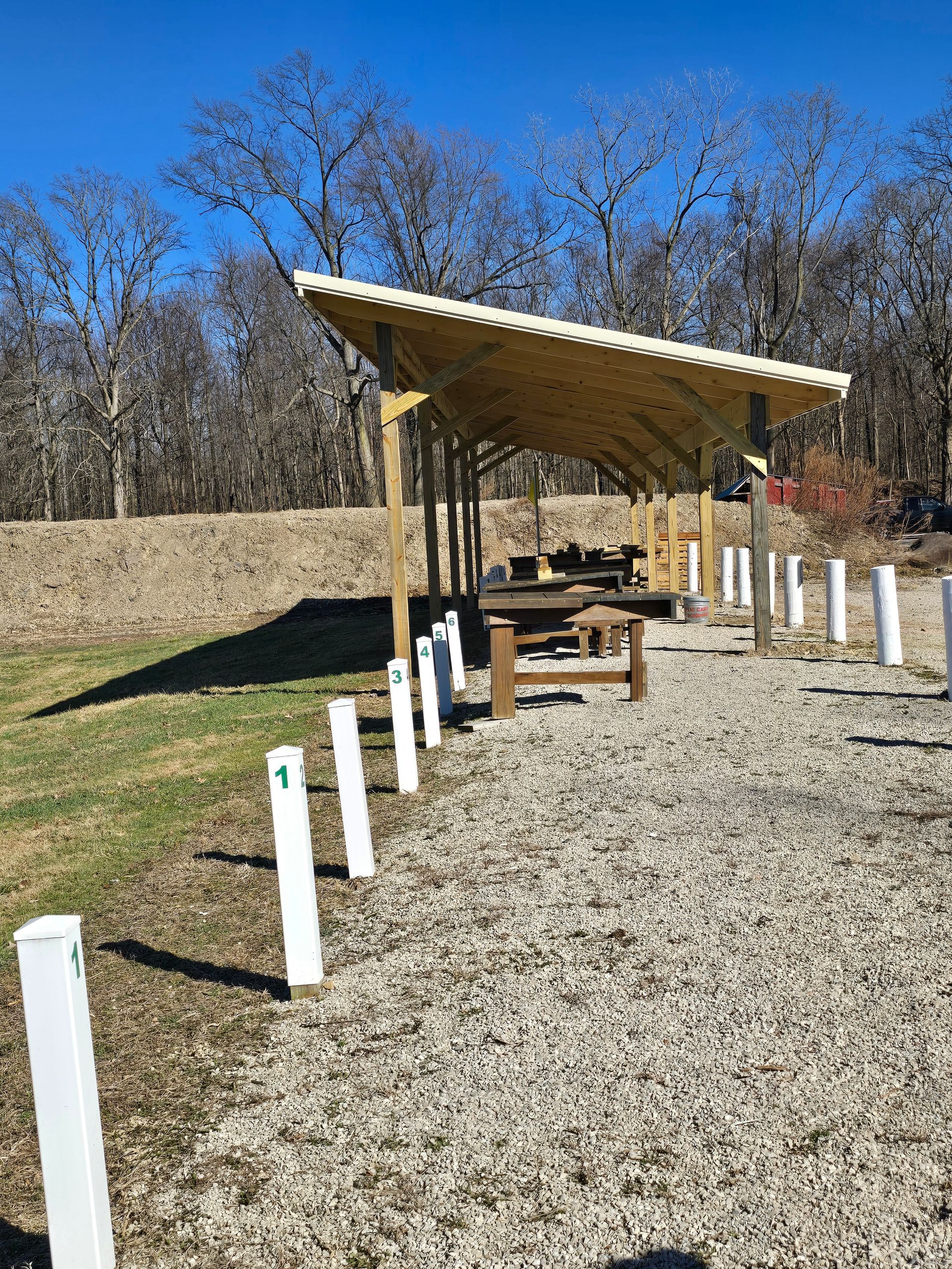 An outdoor shooting range featuring a covered wooden structure and a line of numbered white posts on a gravel path.