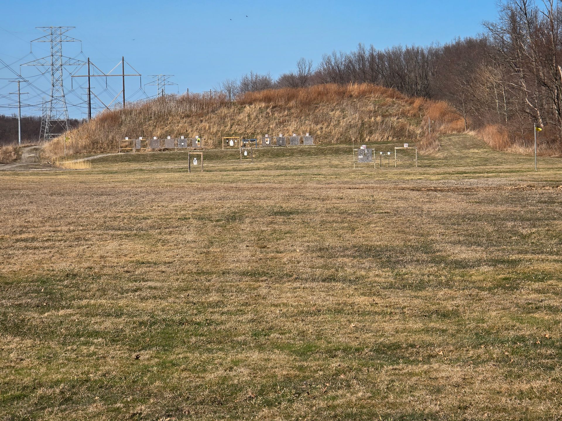 A grassy field leads to a small, raised mound featuring several small, white grave markers under a clear blue sky.