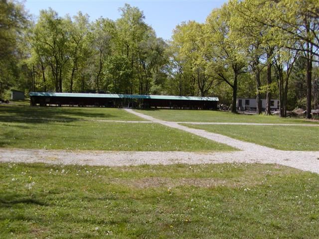 A long, low building with a dark facade sits in a park-like setting with grassy lawns and paved paths under green trees.