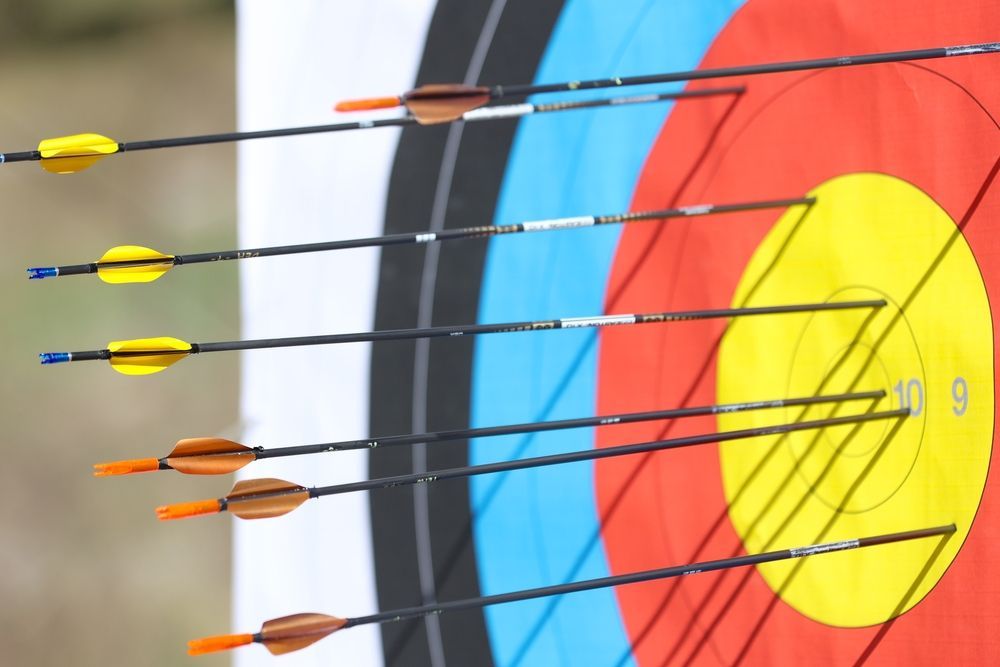 Six arrows with colorful fletching are stuck in an archery target, with most clustered near the center.