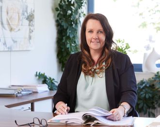 A woman is sitting at a desk reading a book and smiling.