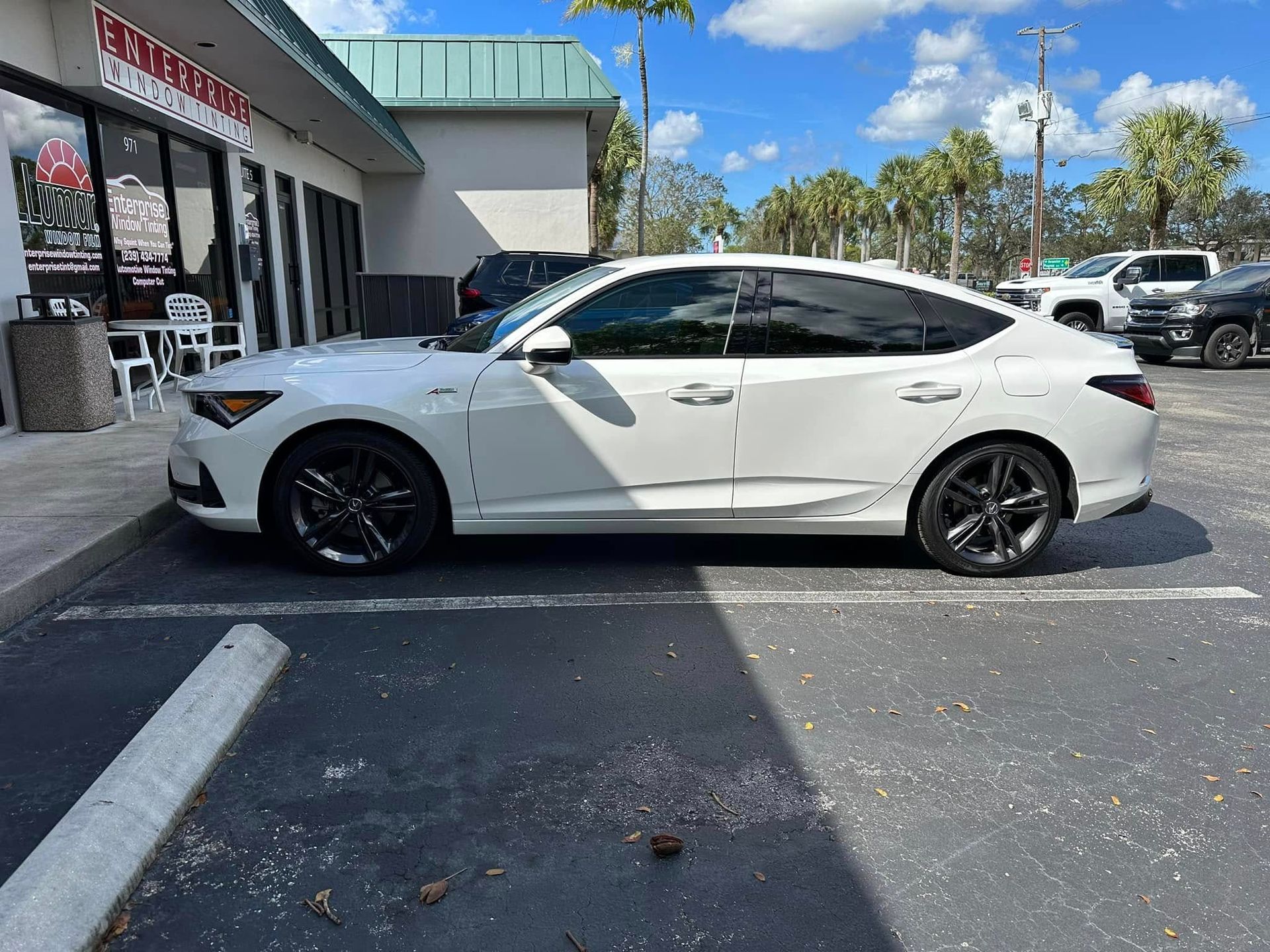 White Acura hatchback with dark side windows, shown in profile outside the tint shop.