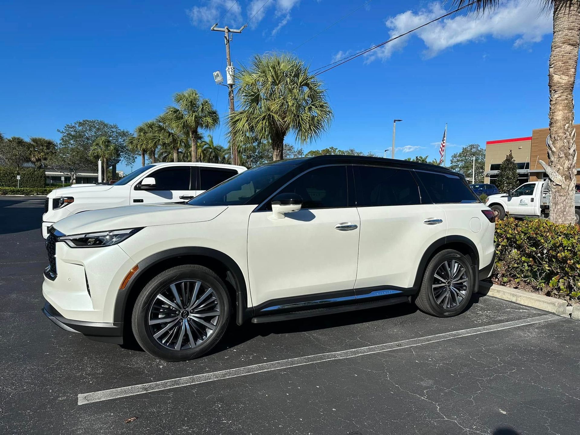 White Infiniti SUV with a black roof and dark side windows, viewed from the front and side.