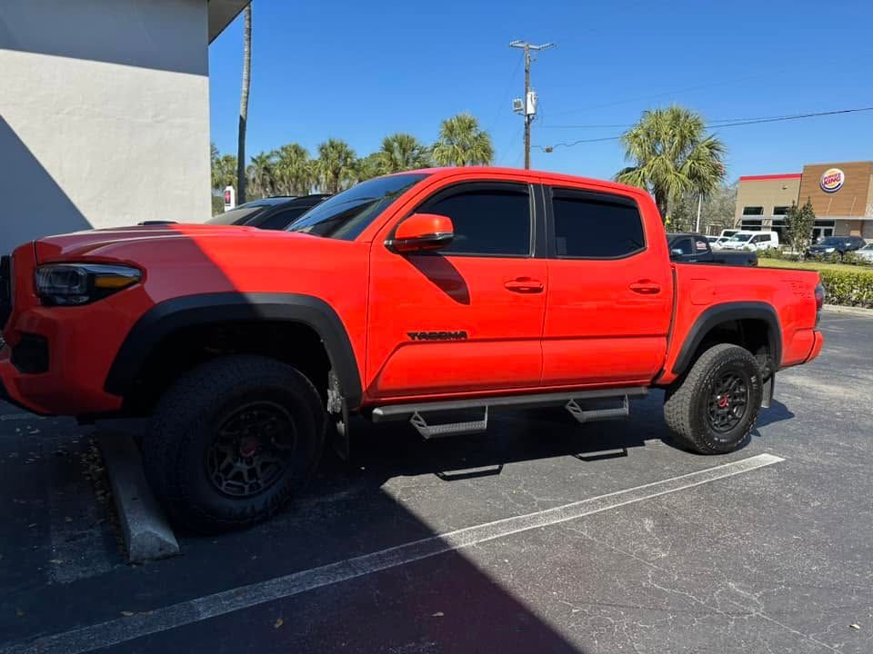 Red Toyota pickup with dark side windows and black wheels, viewed from the front and side.