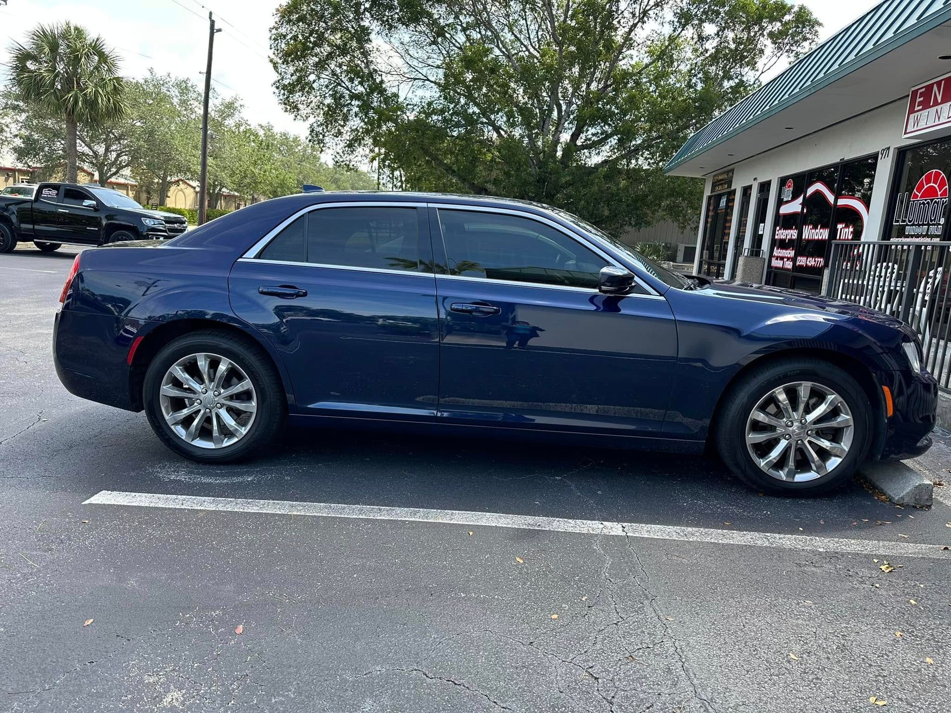 Dark blue Chrysler sedan with dark side windows, shown in profile outside the tint shop.