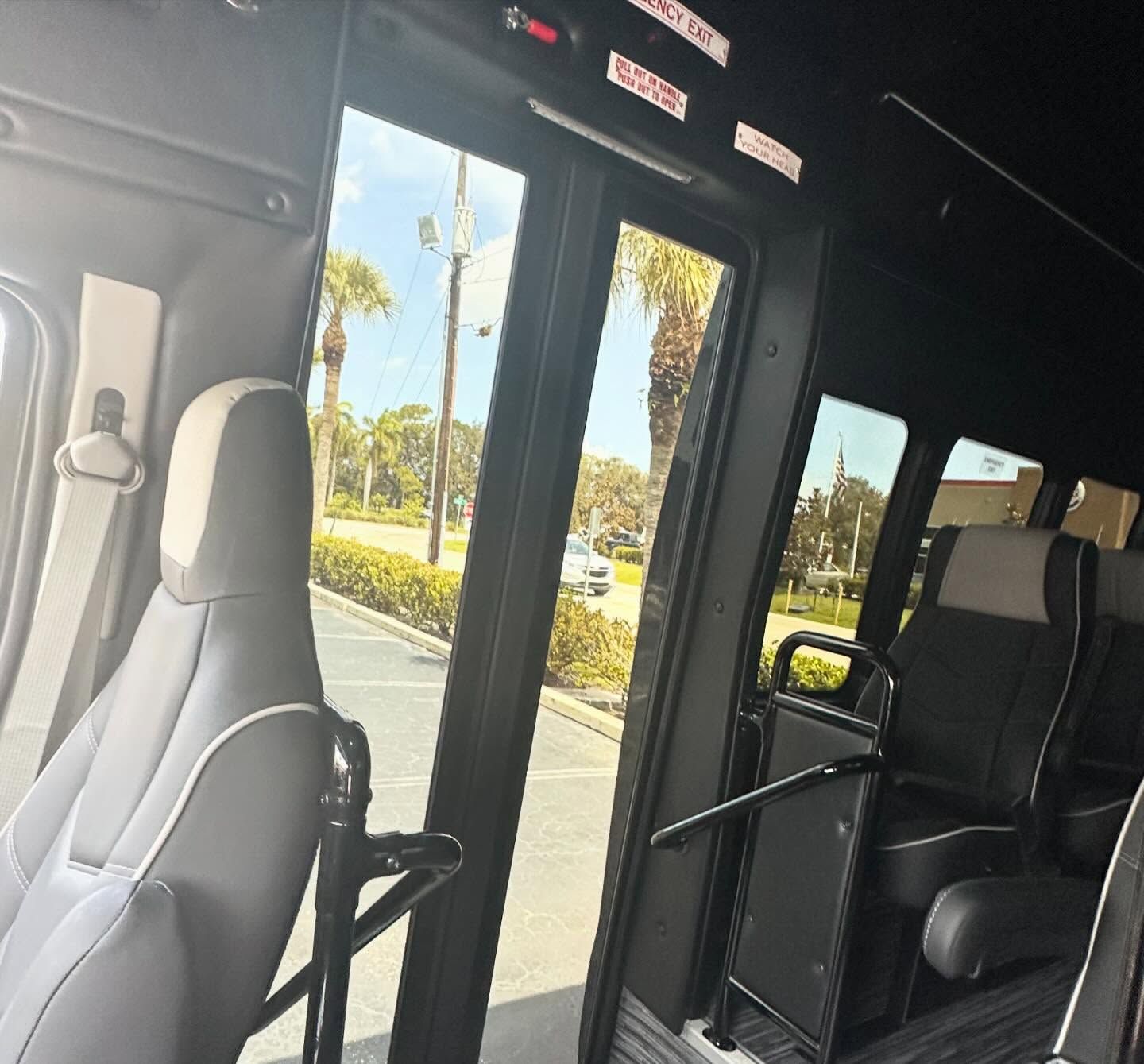 Interior view of a shuttle bus with glass entry doors and black-and-cream passenger seats.