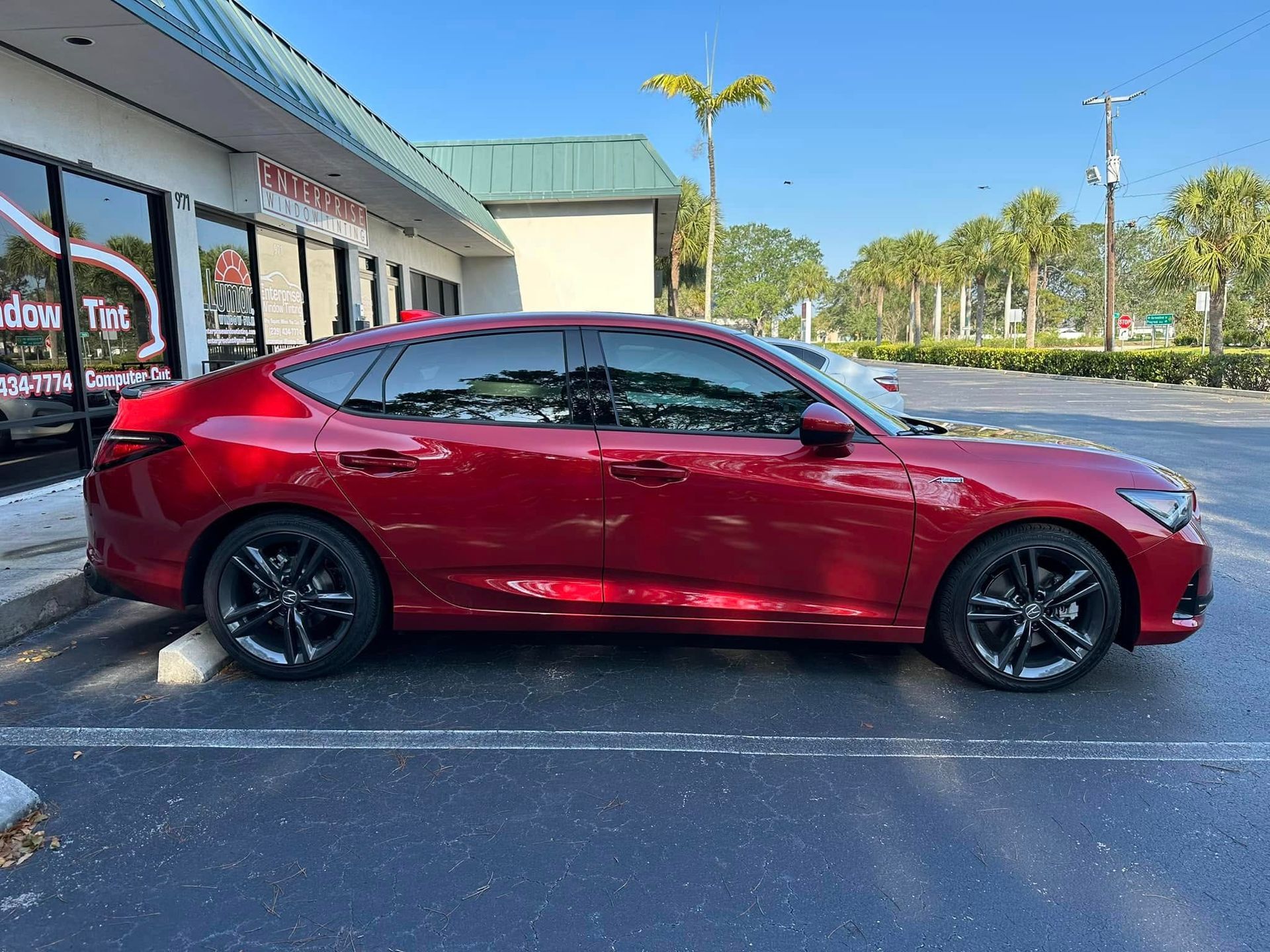 Red Acura hatchback with dark side windows, shown in profile outside the tint shop.