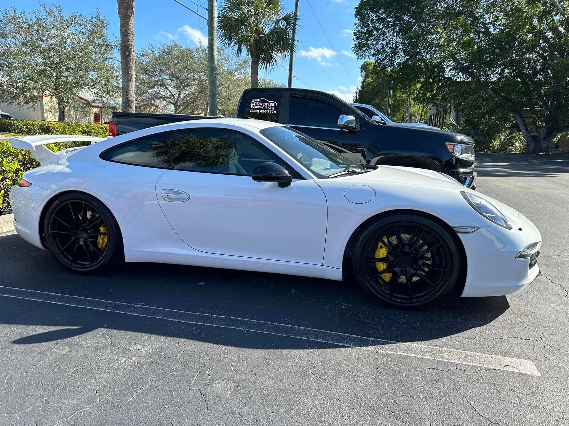 White Porsche sports coupe with dark side windows, black wheels and a rear wing, viewed from the side.