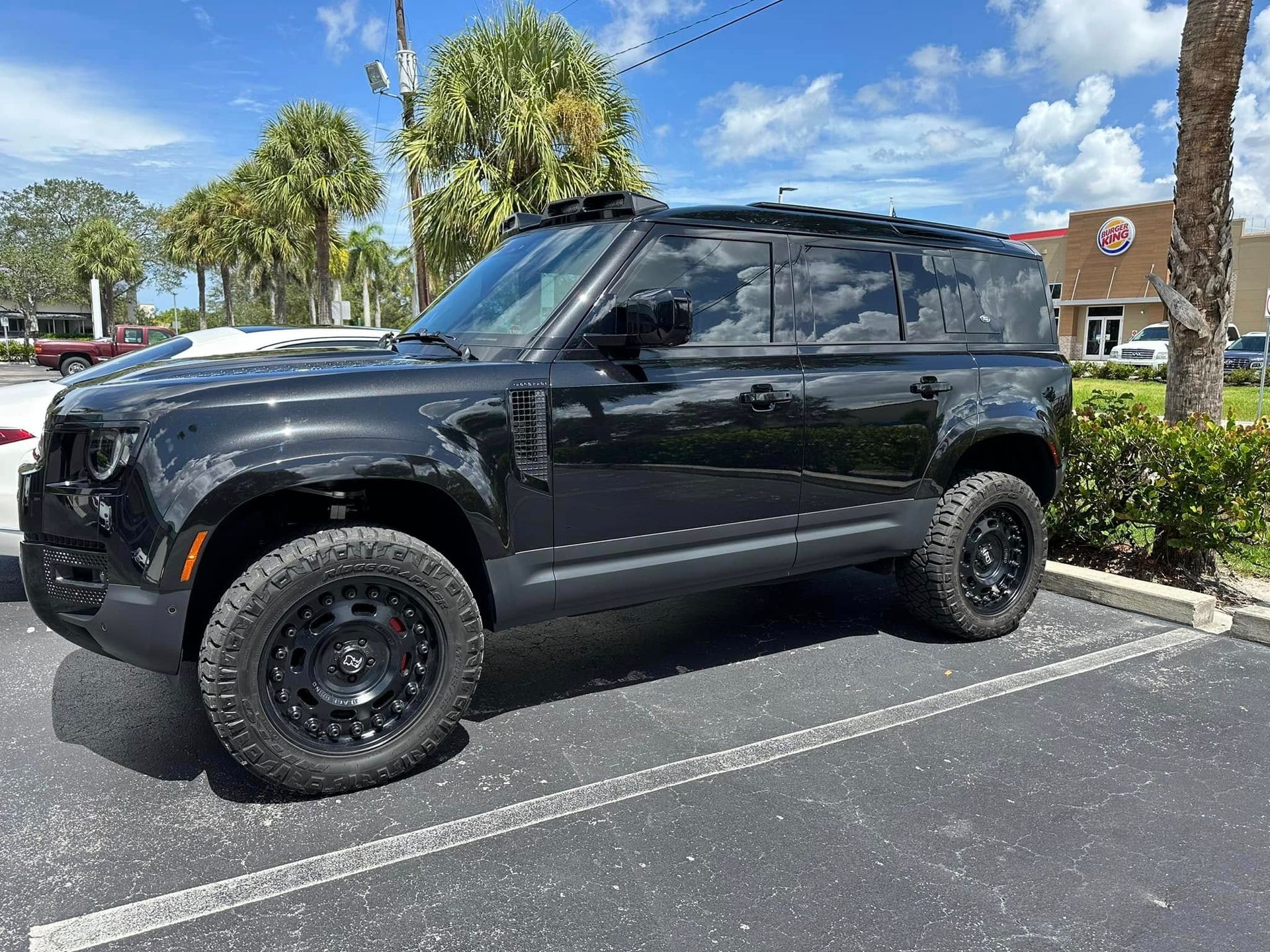 Black Land Rover SUV with dark side windows and off-road tires, viewed from the front and side.