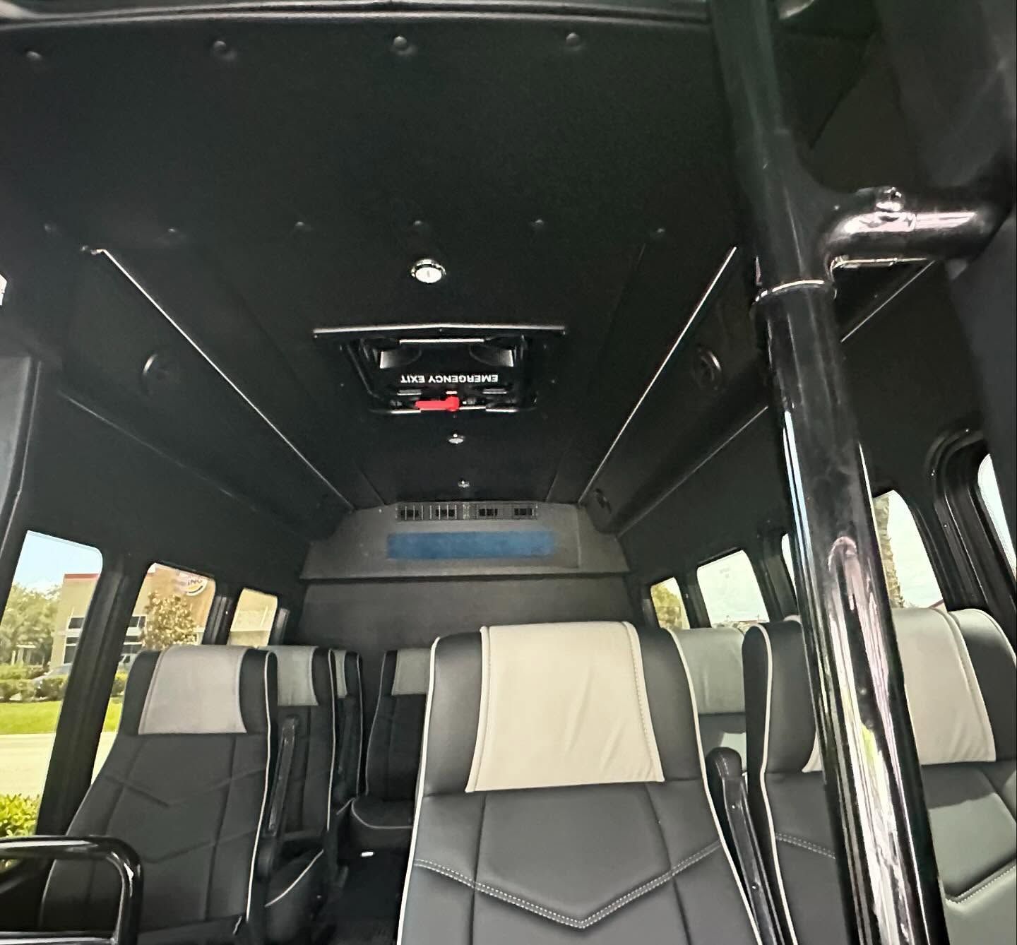 Shuttle bus interior with black-and-cream seats, side windows and a chrome grab pole.