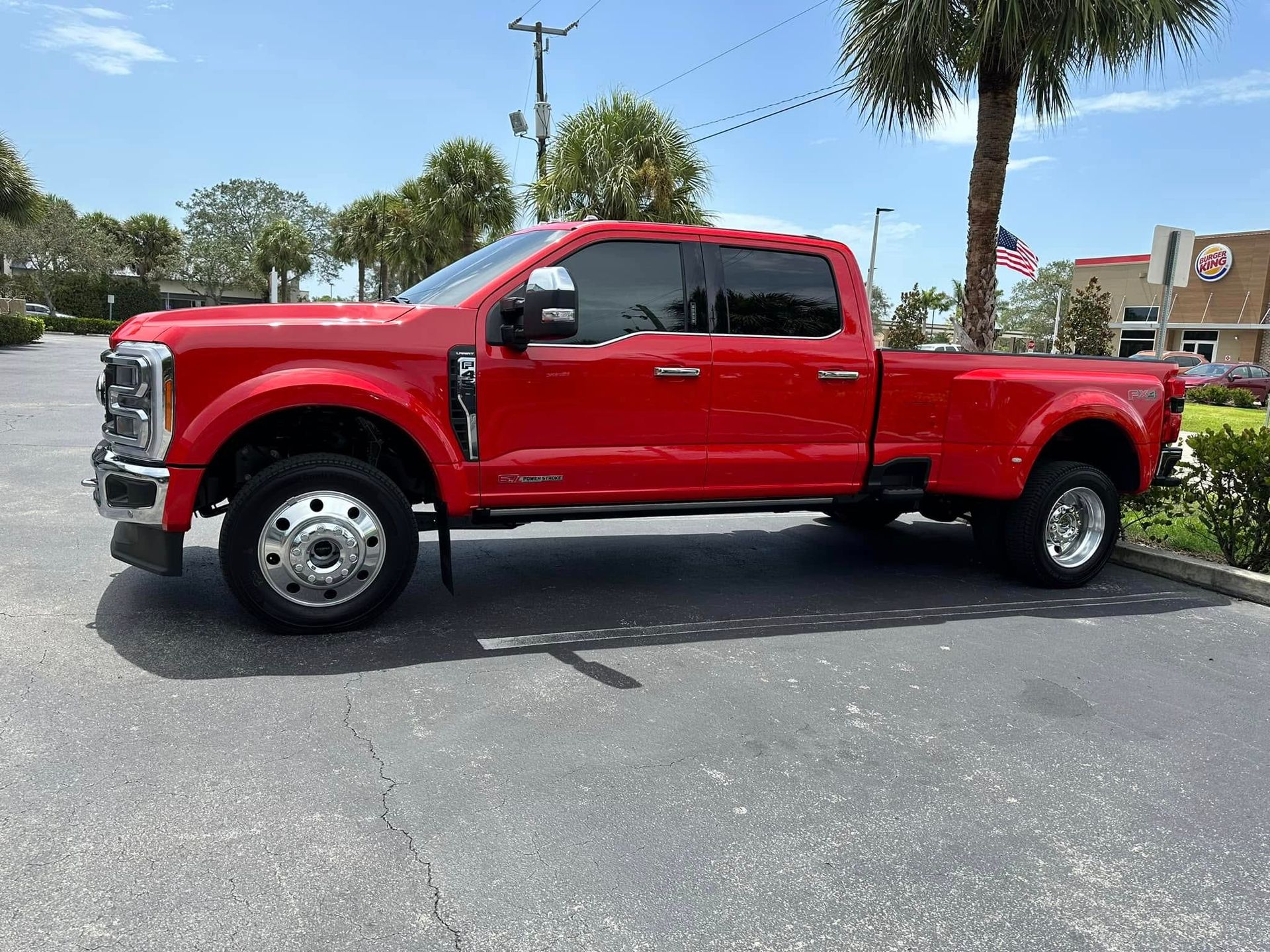 Red Ford crew-cab pickup with dual rear wheels and dark side windows, shown in profile.