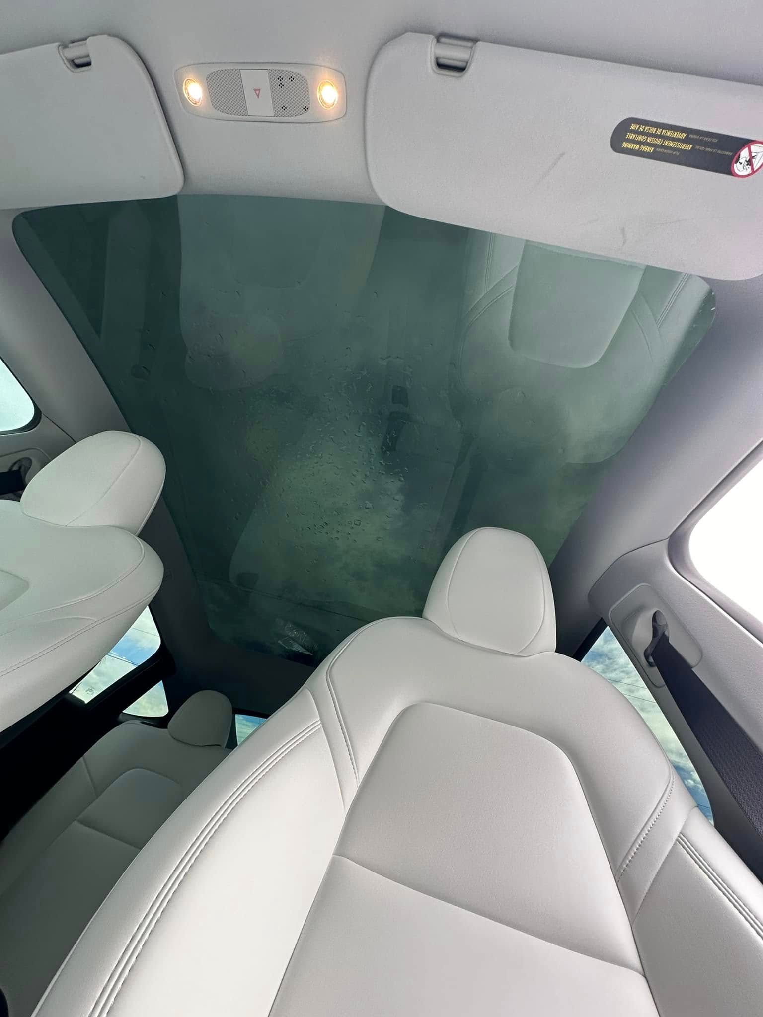 Interior view of a car’s panoramic glass roof above white seats.