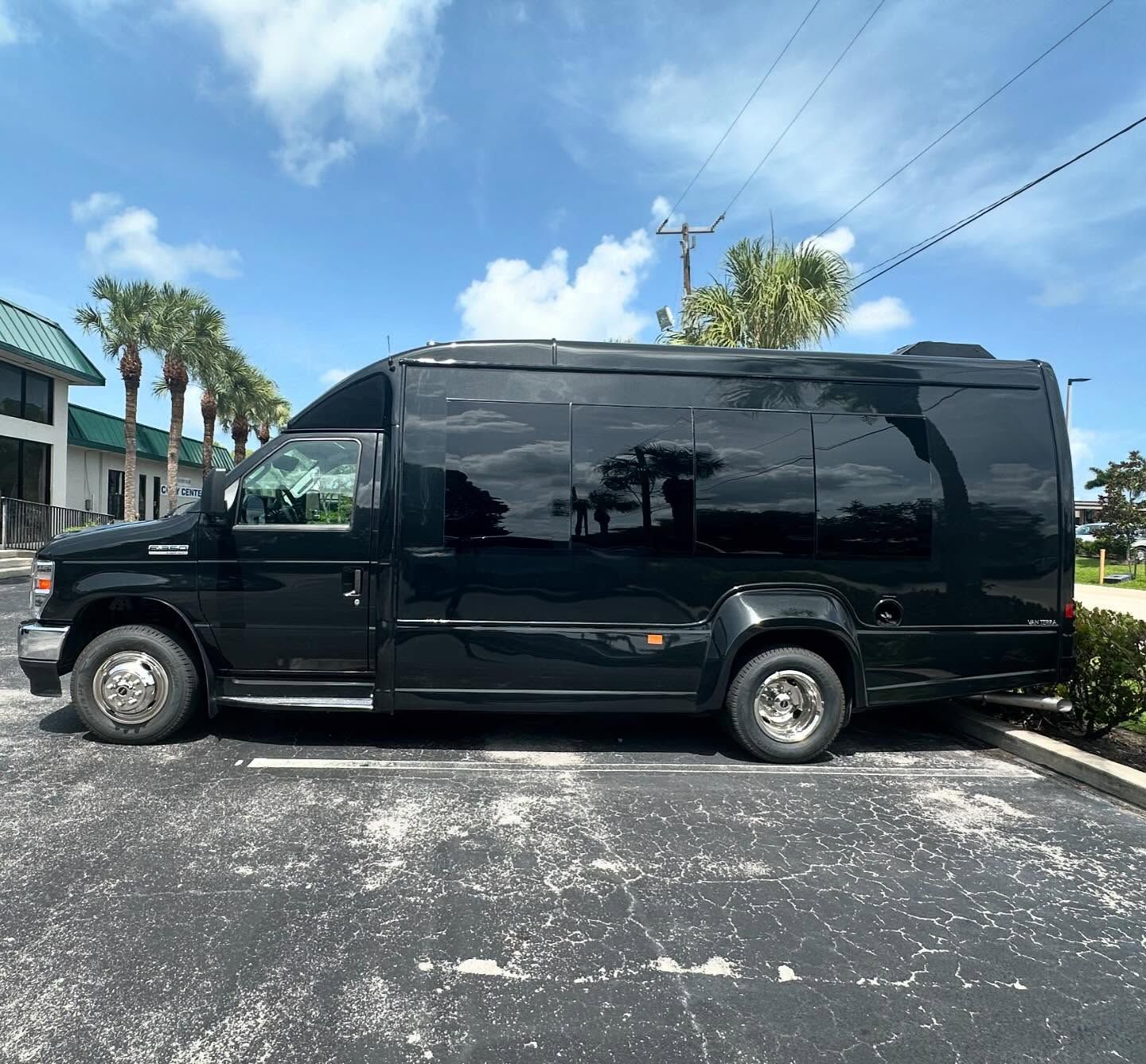 Black passenger shuttle with dark side windows, shown in profile in a parking lot.
