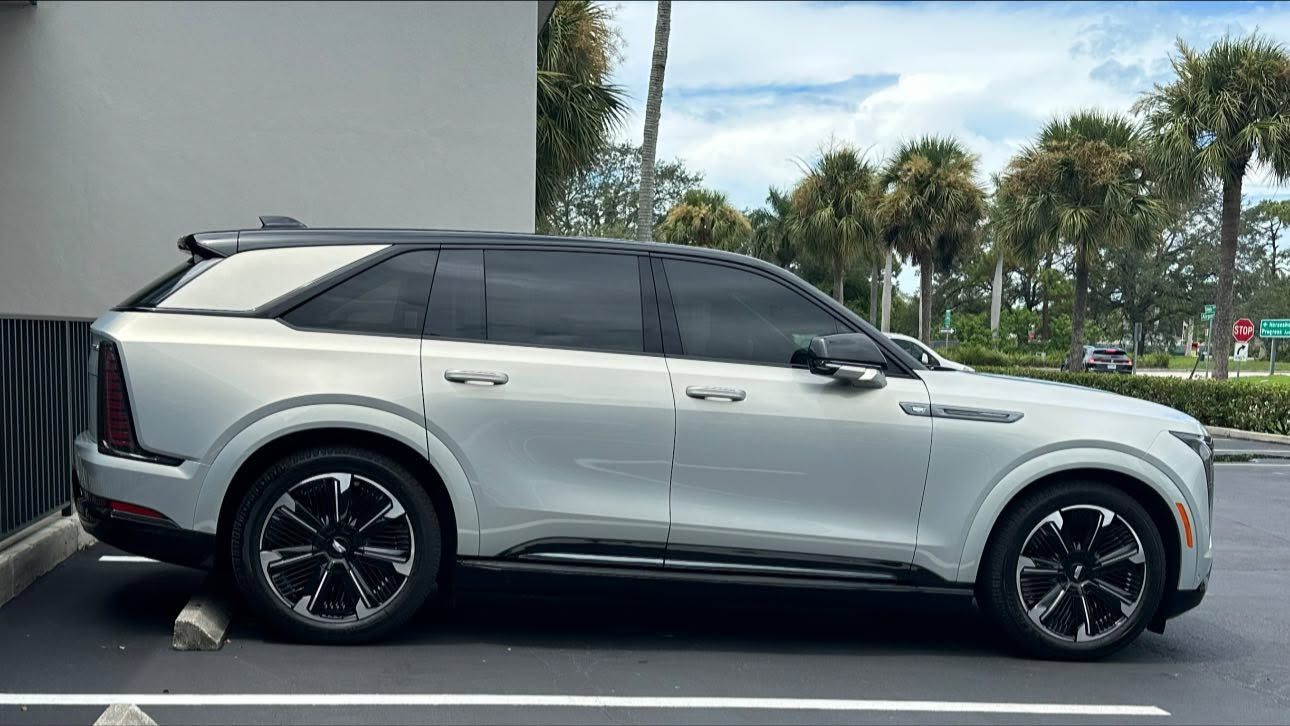 Silver Cadillac SUV with a black roof and dark side windows, shown in profile.
