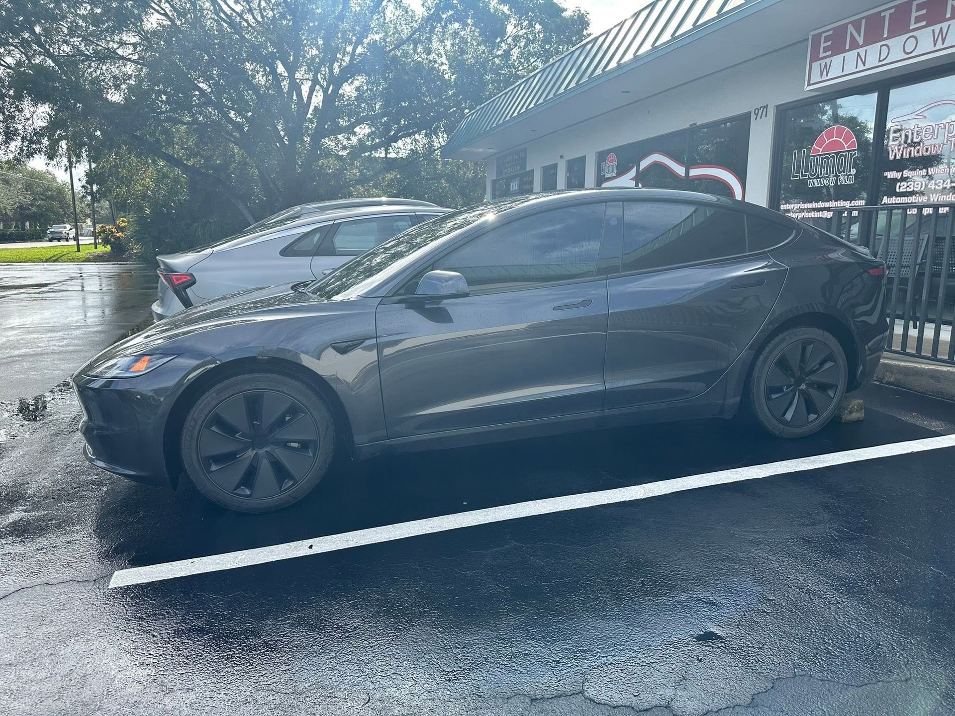 Gray Tesla sedan with dark side windows, parked outside Enterprise Window Tinting.