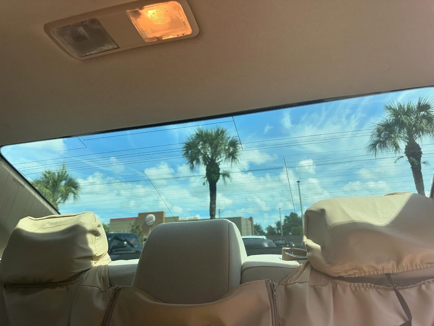View through a car’s rear window above beige rear seats and covered headrests.