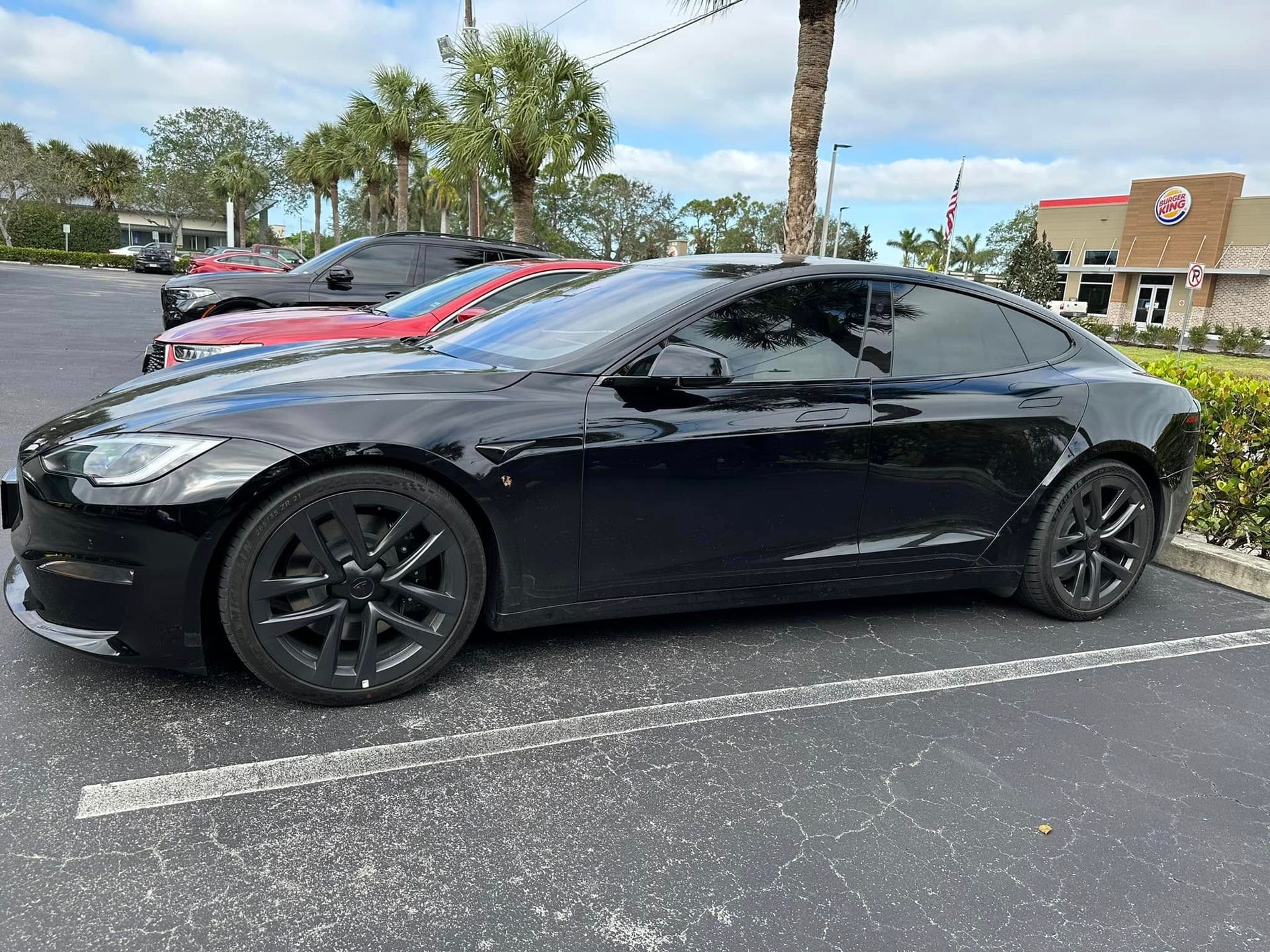 Black Tesla sedan with dark side windows and black wheels, viewed from the front and side.