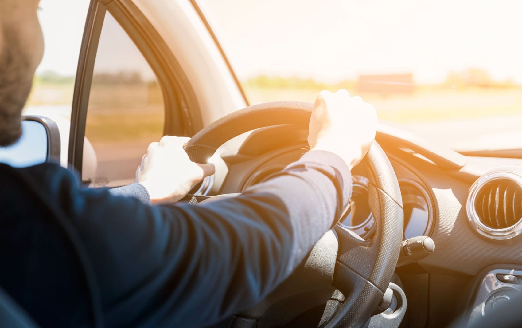 Driver holding a steering wheel as bright sunlight enters through the windshield.