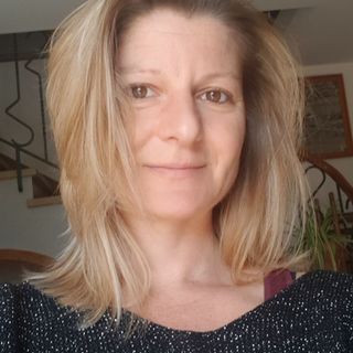 Une femme aux cheveux blonds porte un pull noir et sourit.