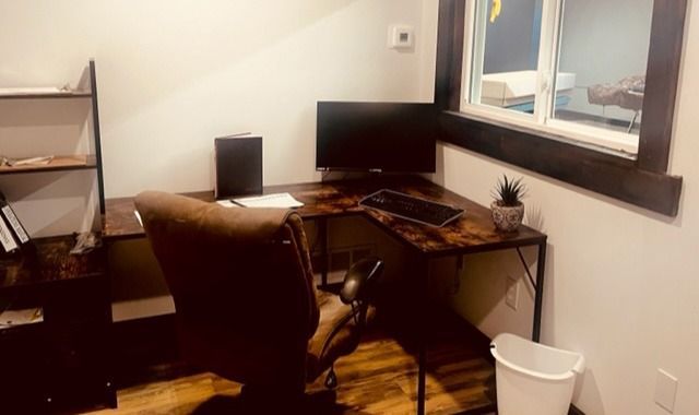 Small home office with desk, monitor, chair, shelf, and window overlooking the room