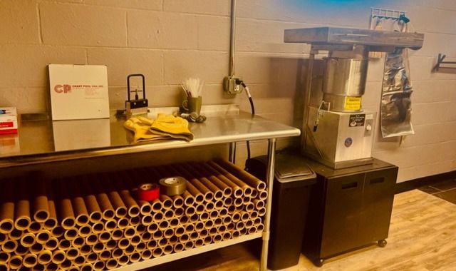 Restaurant prep station with countertop, storage rack of cups, cleaning supplies, and a beverage machine on black cabinets