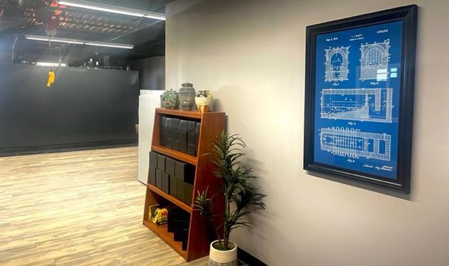 Modern office lobby with wood floor, black wall, bookshelf, plant, and framed blue poster