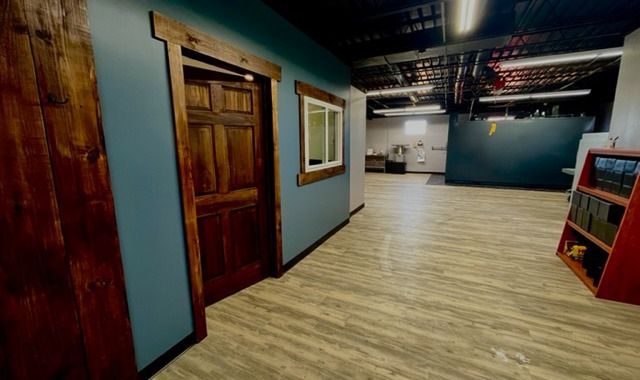 Empty hallway with wooden floor, blue walls, a closed wooden door, and framed wall art.