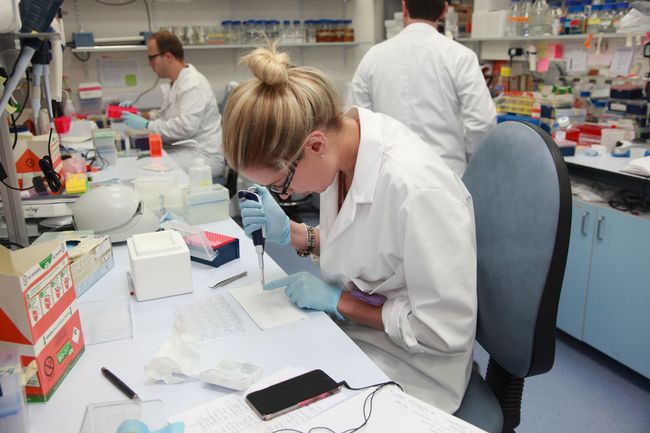 A woman in a lab coat is working on a cell phone