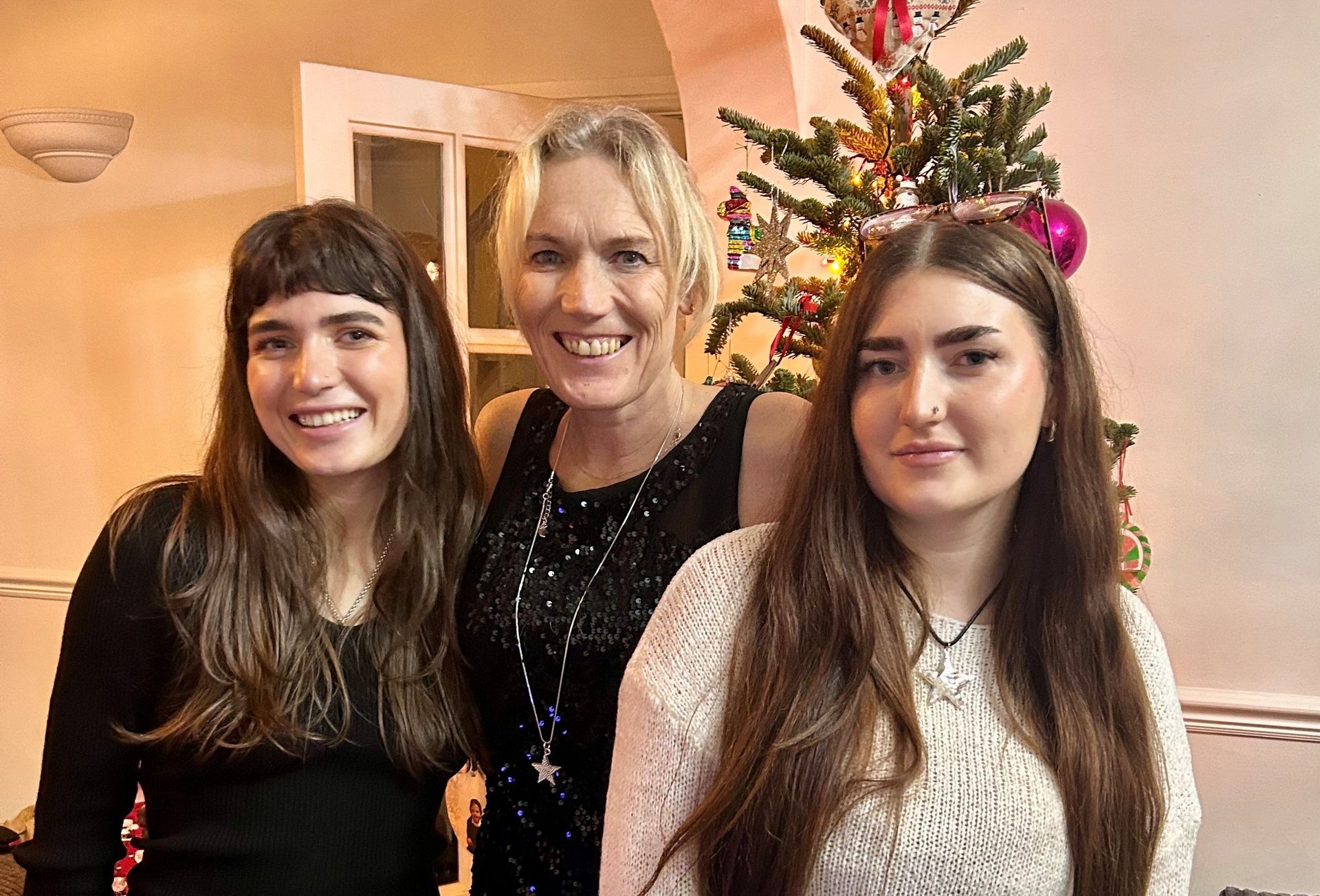 Jane and her two daughters smiling in front of a Christmas tree