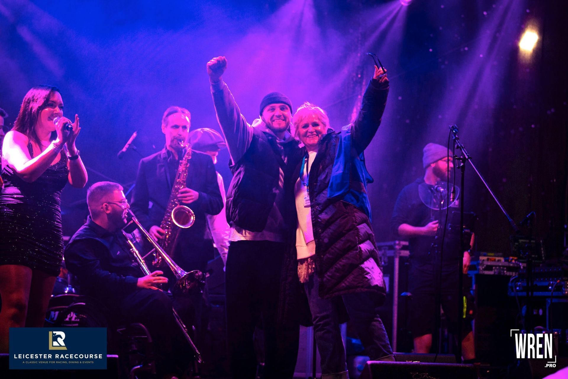 A group of people are standing on a stage with their arms in the air.