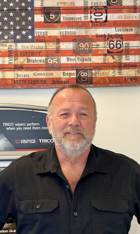 A man with a beard is standing in front of an american flag.
