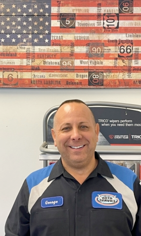 A man in a blue and white shirt is smiling in front of an american flag.