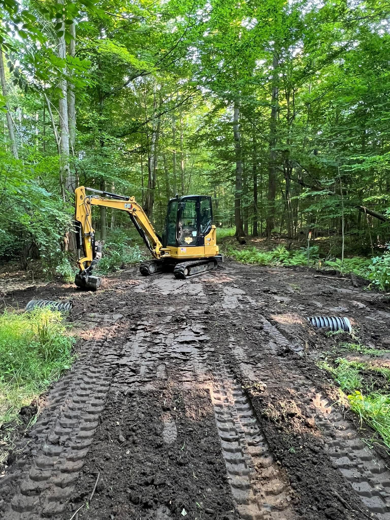 Yellow excavator on a muddy path in a wooded area.