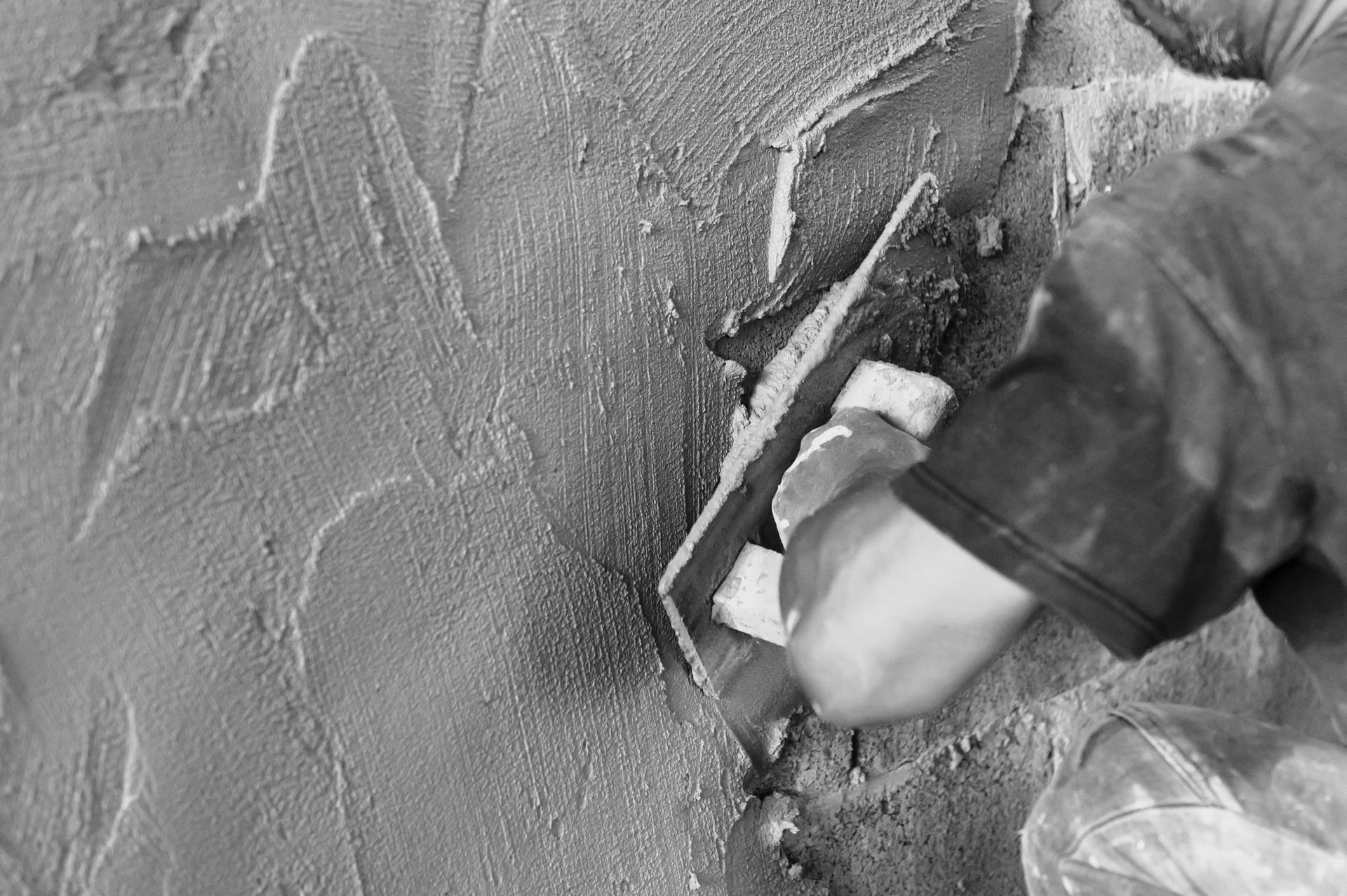Une photo en noir et blanc d'une personne utilisant une truelle sur un mur.