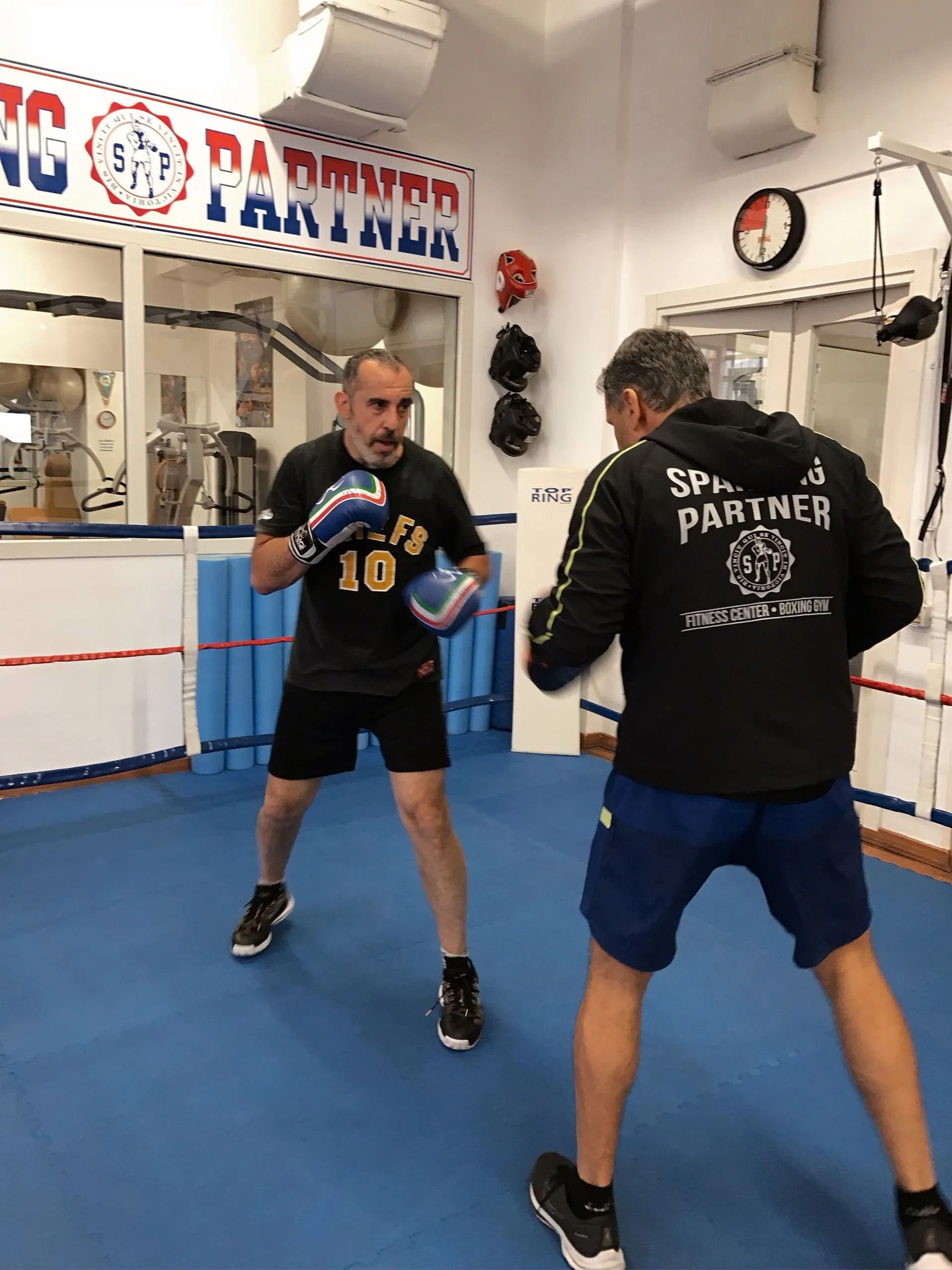 Due persone si allenano in una palestra di pugilato, una con i guantoni in mano e l'altra di fronte a lui