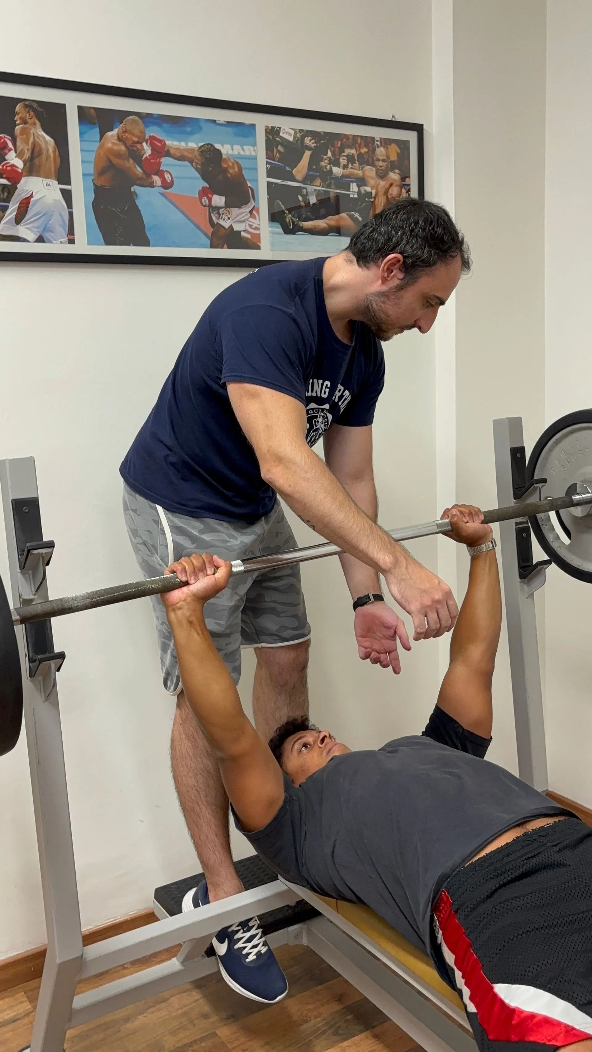 Un assistente aiuta un uomo a sollevare un bilanciere su una panca in palestra.