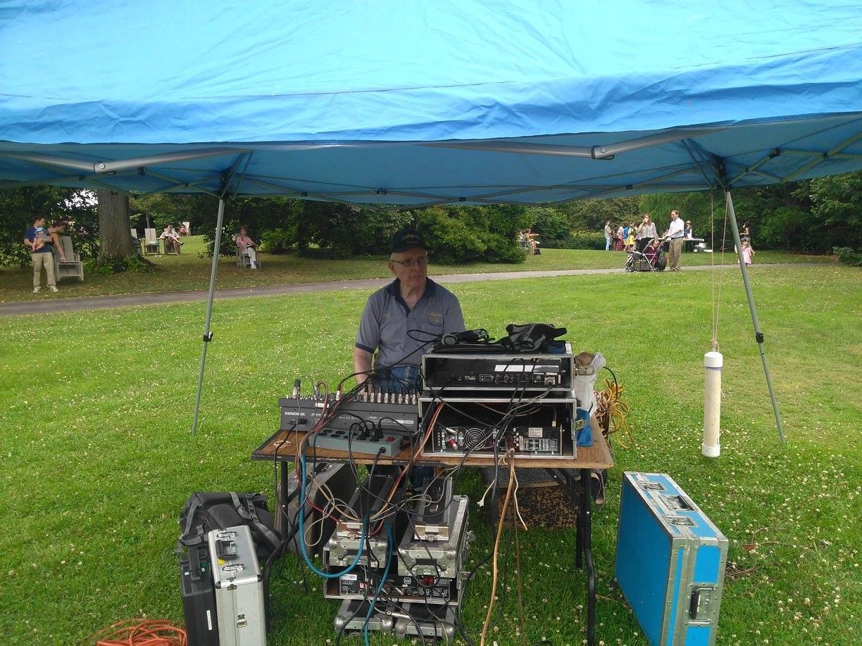 Man operating audio equipment under a blue tarp at an outdoor park event