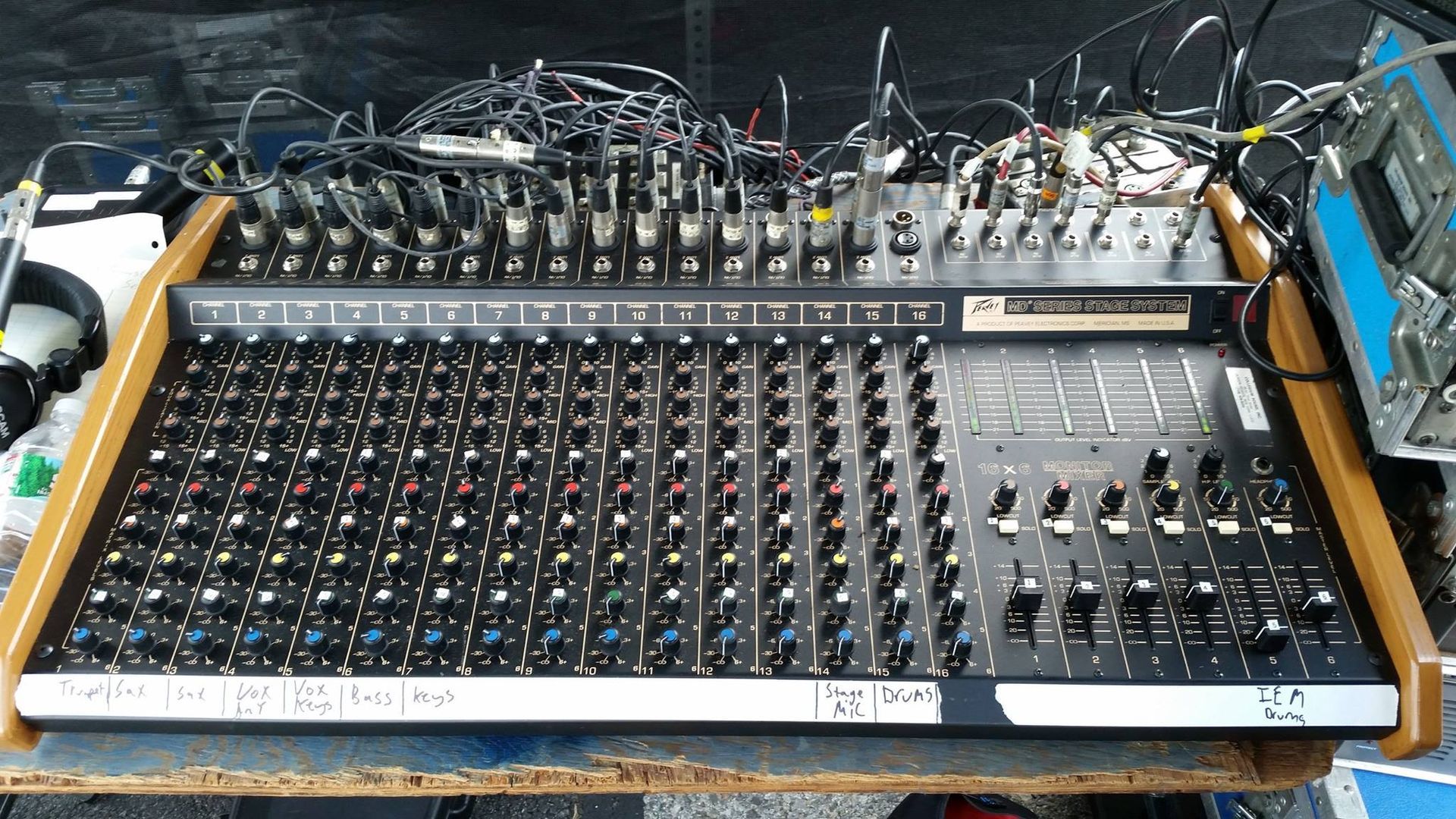 Audio mixing console with many knobs, sliders, and cables on a workbench