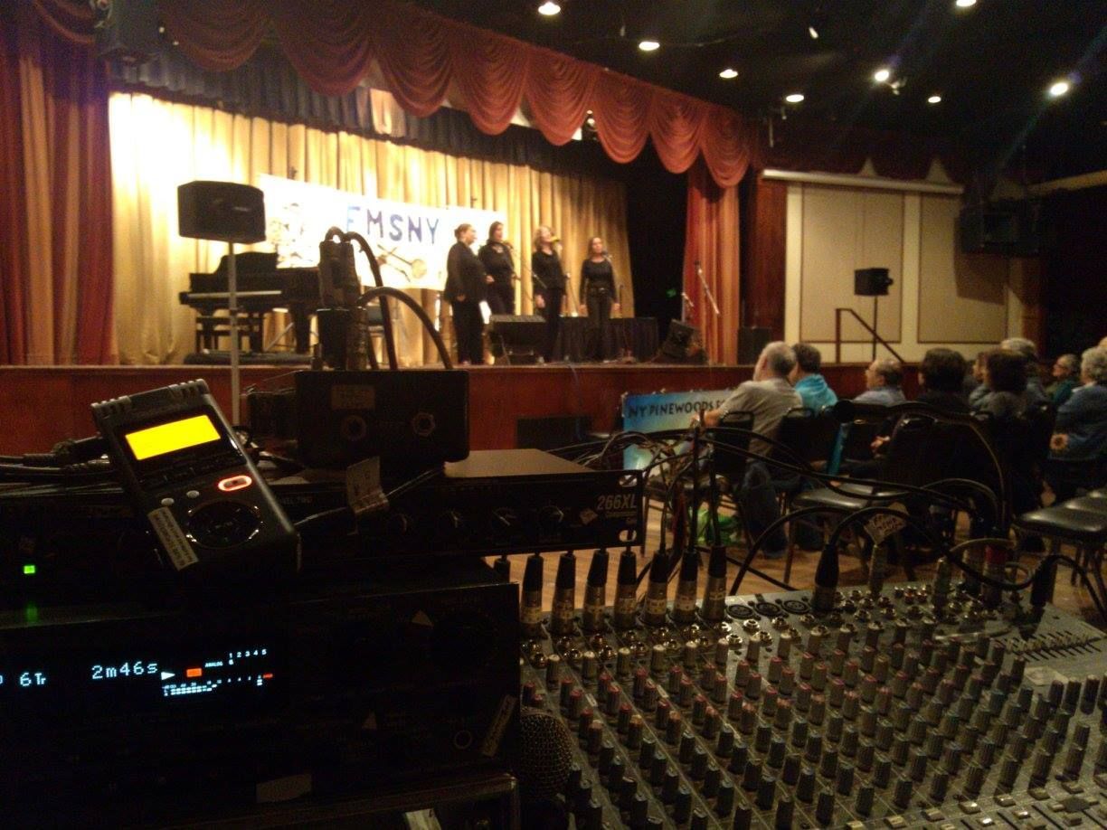 Indoor stage performance with musicians under warm lights, viewed from a sound mixer in the audience area