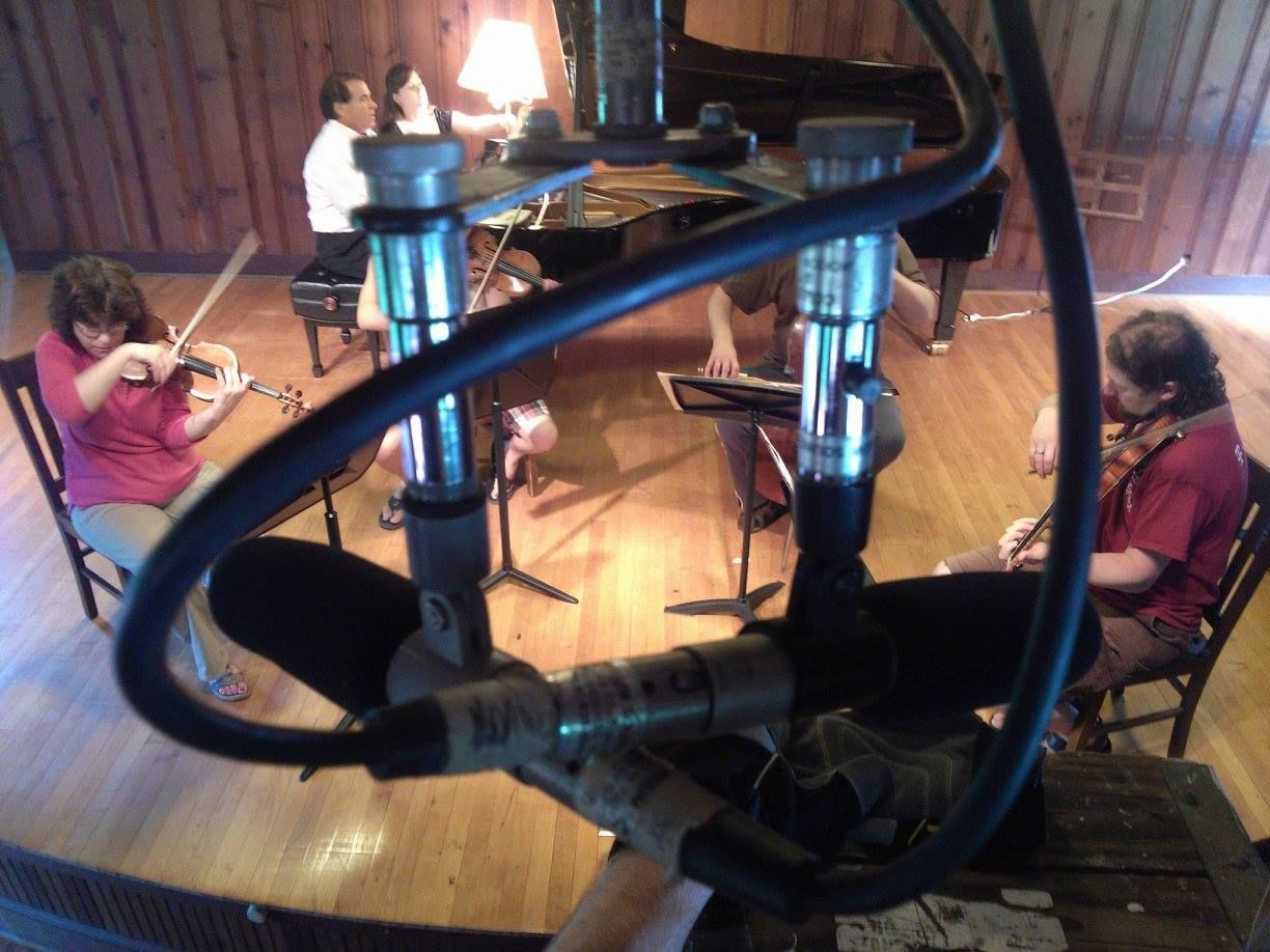 Musicians rehearsing in a cozy room with violin, piano, and guitars around a round table