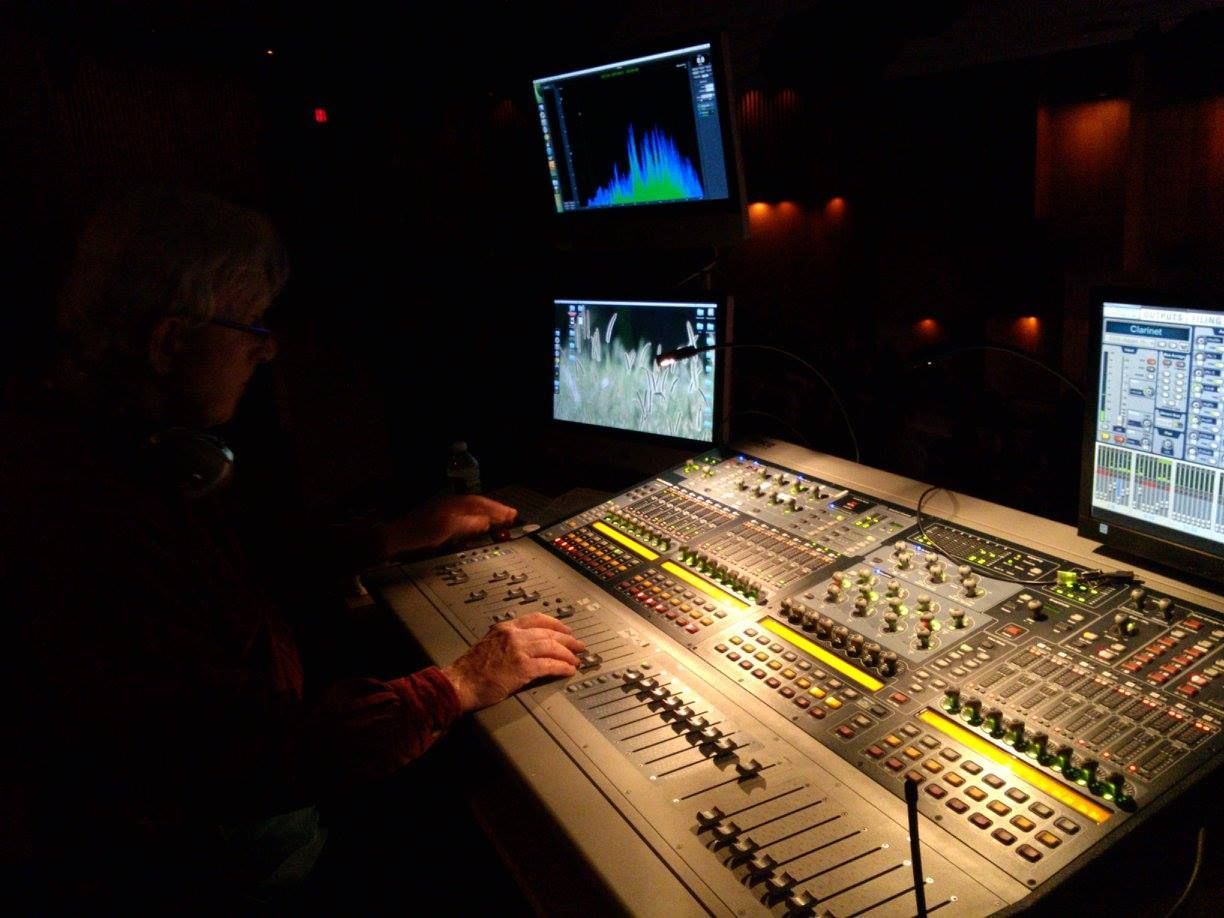 Audio engineer mixing sound at a studio console with dual monitors in a dimly lit control room