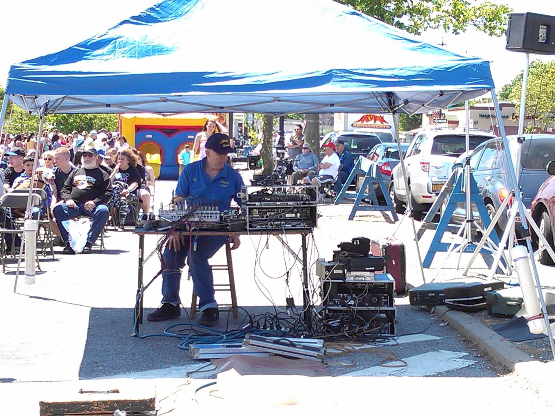 Street musician performing under a blue canopy at an outdoor market, with equipment and crowds nearby