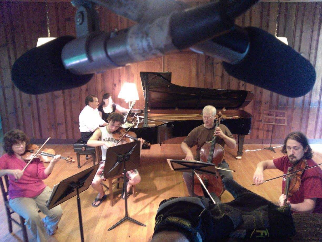 String quartet playing in a studio with a grand piano and overhead microphones