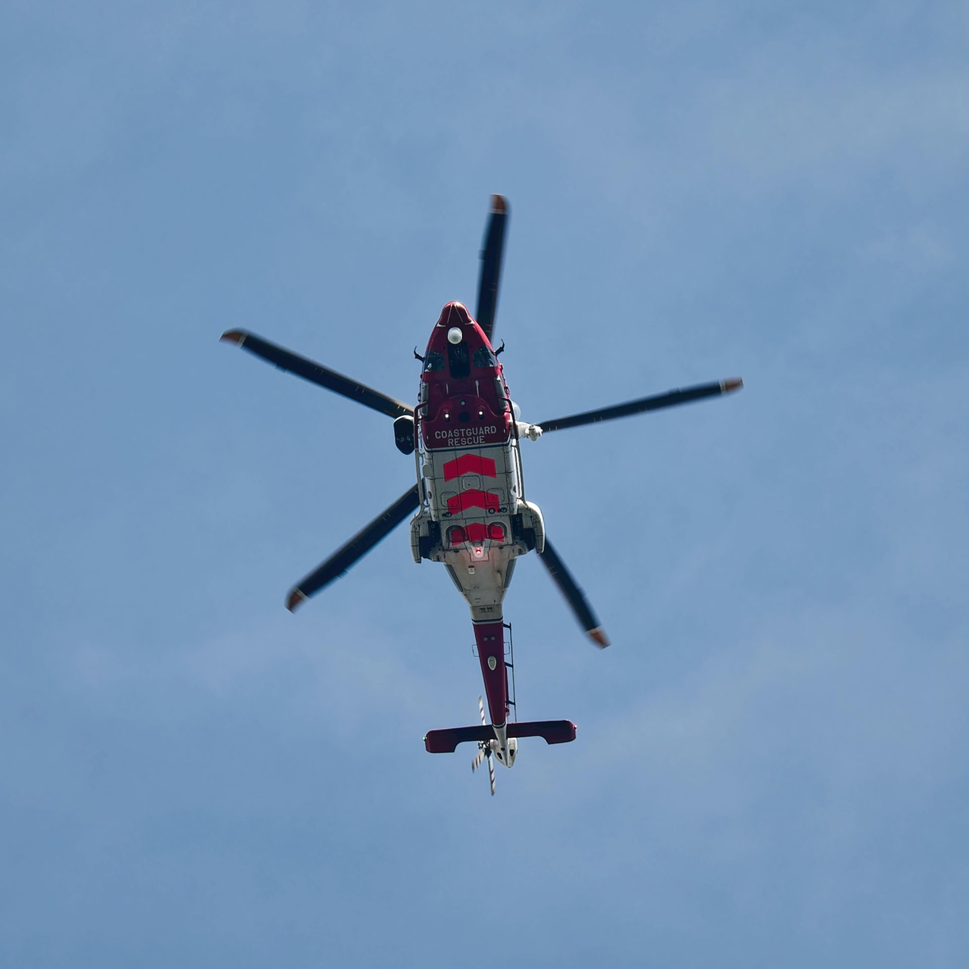 A red and white helicopter is flying through a blue sky